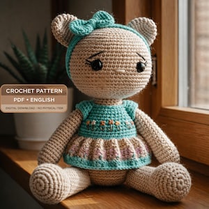 Może przedstawiać: Ręcznie robiona szydełkowa lalka w kształcie misia z turkusową kokardą, opaską na głowę i sukienką. Sukienka ma haftowane kwiaty i różowo-beżową spódnicę. Lalka siedzi na drewnianej powierzchni w pobliżu okna. Tekst na zdjęciu brzmi "CROCHET PATTERN PDF • ENGLISH DIGITAL DOWNLOAD • NO PHYSICAL ITEM".