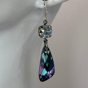May include: A single, elegant earring with a silver-tone hook. The earring features a round, iridescent crystal above a larger, teardrop-shaped crystal with shades of teal, purple, and green. Jewelry.