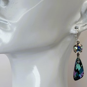 May include: A pair of dangle earrings featuring iridescent crystals. Each earring has a square-cut crystal at the top and a teardrop-shaped crystal below. The crystals display a range of colors, including green, blue, and purple, and are set in a silver-tone metal.