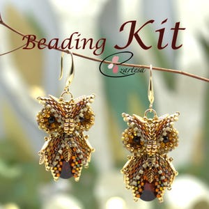 Könnte beinhalten: Ein Perlen-Set zum Basteln einer Paar Eulenohrringe. Die Eulen sind aus braunen, goldenen und weißen Perlen gefertigt und haben schwarze Augen. Die Ohrringe hängen an goldenen Haken.