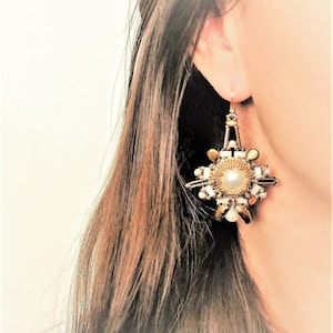 May include: A pair of gold and white beaded earrings with a large pearl in the center of each earring. The earrings are shaped like a star.