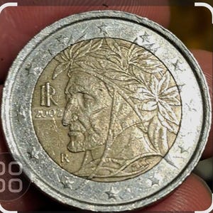 Puede incluir: Una moneda de 1 euro de color plateado y dorado con el retrato de un hombre con una corona de laurel en la cabeza. La moneda tiene el texto "2002" y "R" en ella.