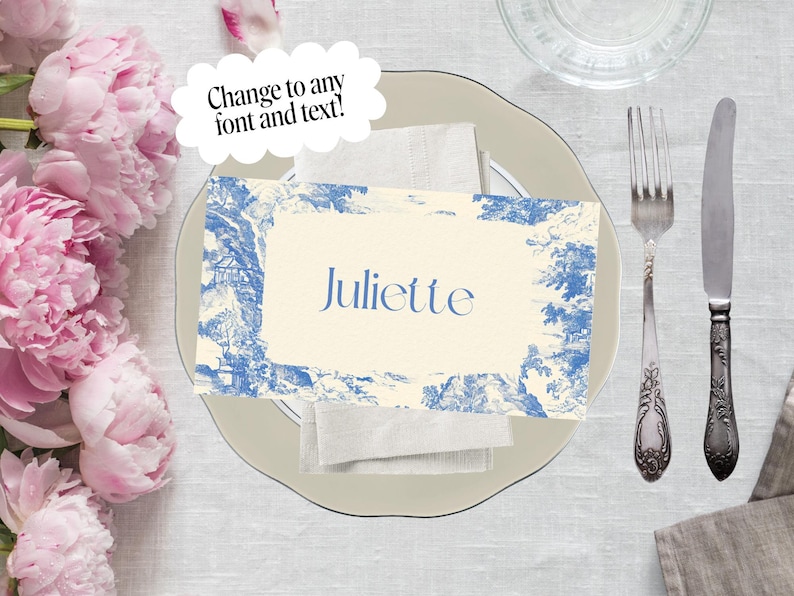 Puede incluir: Un cubierto con una tarjeta de sitio de estilo toile de Jouy azul y blanco que dice "Juliette". La tarjeta est&aacute; sobre una servilleta blanca, un plato gris claro y junto a un tenedor y un cuchillo. El texto "&iexcl;Cambia a cualquier fuente y texto!" est&aacute; en una burbuja.