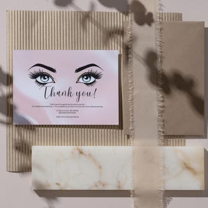 May include: A thank you card with a pink and white background features illustrated eyes with long lashes. The words "Thank you!" are written in elegant script. The card is on a textured background with other decorative elements.