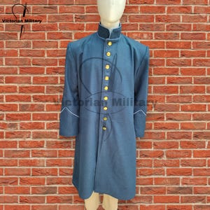 Puede incluir: Una larga levita azul oscuro con cuello alto y botones dorados. La levita tiene ribetes blancos en las mangas y está hecha de una tela gruesa de lana.