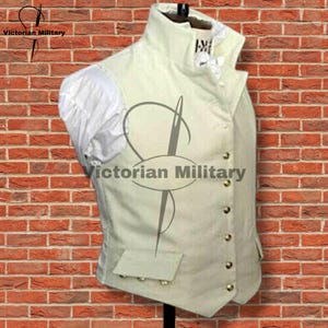 May include: An off-white vest featuring a high collar, a row of metallic buttons down the front, and two flap pockets at the waist. The garment is layered over a white shirt with gathered sleeves. The text Victorian Military is visible.
