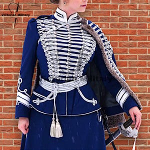 Puede incluir: Chaqueta militar azul marino con ribetes blancos y detalles plateados. La chaqueta presenta cuello alto, trenzado decorativo y cinturón a juego. Una capa forrada de piel está sobre los hombros. Se ve el texto "Victorian Military".