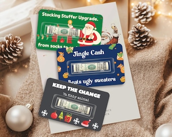 Puede incluir: Tres tarjetas de regalo navideñas con billetes enrollados. La tarjeta verde dice "Stocking Stuffer Upgrade", la azul "Jingle Cash" y la negra "KEEP THE CHANGE". Diseños festivos.
