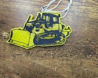 May include: A yellow and black bulldozer-shaped ornament with a white string for hanging. The bulldozer has a detailed design, including the blade, tracks, and cab. The ornament is likely made of a lightweight material.