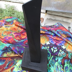 May include: A matte black sculptural object with a tall, tapered, and twisted vertical form mounted on a square base. The word PRESENCE is embossed on the front of the base, and additional small text is visible on the side of the base.