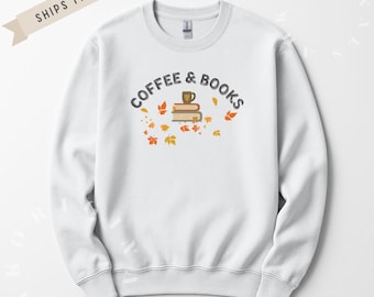 May include: White sweatshirt with the text "COFFEE & BOOKS" in a circular design, featuring a coffee cup and books graphic. Autumn leaves in orange, yellow, and brown surround the text. The sweatshirt has a crew neck and long sleeves. The words "SHIPS FAST" are on a banner.
