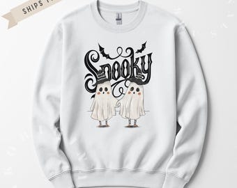 Może przedstawiać: Biała bluza z motywem Halloween. Projekt przedstawia dwa kreskówkowe duszki w kapeluszach, z napisem "Spooky" nad nimi w stylizowanej czcionce. Bluza ma okrągły dekolt.