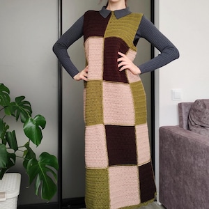 Può includere: Abito all'uncinetto patchwork fatto a mano nei toni del marrone, verde oliva e rosa. L'abito senza maniche ha un colletto e un orlo al ginocchio. L'abito è indossato sopra un top grigio a maniche lunghe e abbinato a stivali neri.