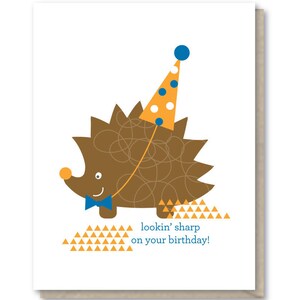 May include: A birthday card featuring a brown hedgehog wearing a blue and white party hat with a blue bow tie. The hedgehog is standing on a background of orange triangles. The card reads "lookin' sharp on your birthday!"