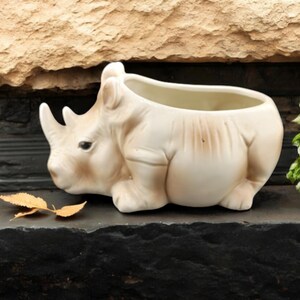 May include: A set of three ceramic mugs with a speckled, matte finish. The mugs are in shades of cream, light gray, and dark gray. Each mug has a simple, minimalist design and a rounded handle.