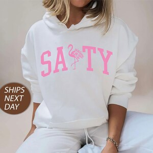 a woman wearing a white sweatshirt with a pink flamingo on it