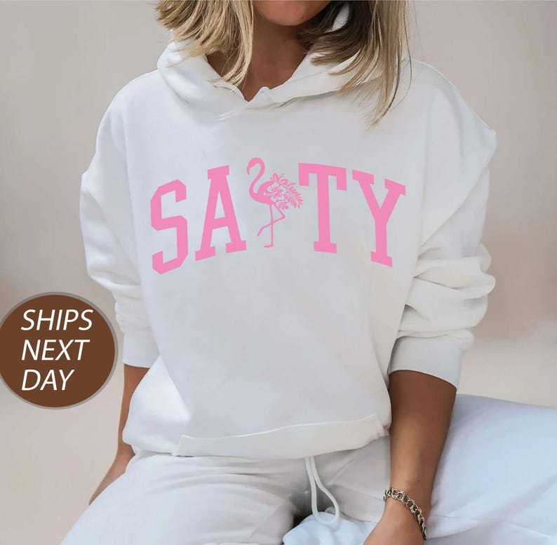 a woman wearing a white sweatshirt with a pink flamingo on it