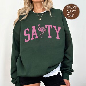 a woman wearing a green sweatshirt with pink flamingos on it