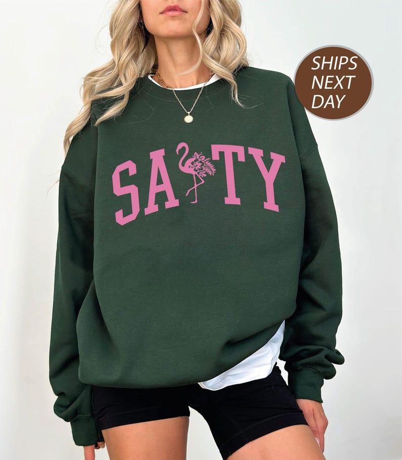 a woman wearing a green sweatshirt with pink flamingos on it