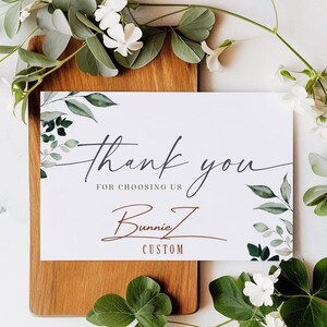 a thank card with greenery on a cutting board