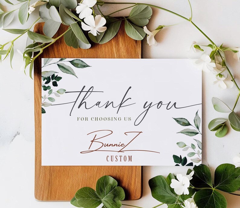 a thank card with greenery on a cutting board