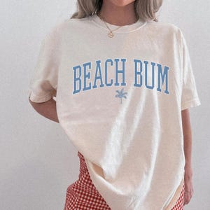 a woman wearing a beach bum t - shirt and checkered shorts