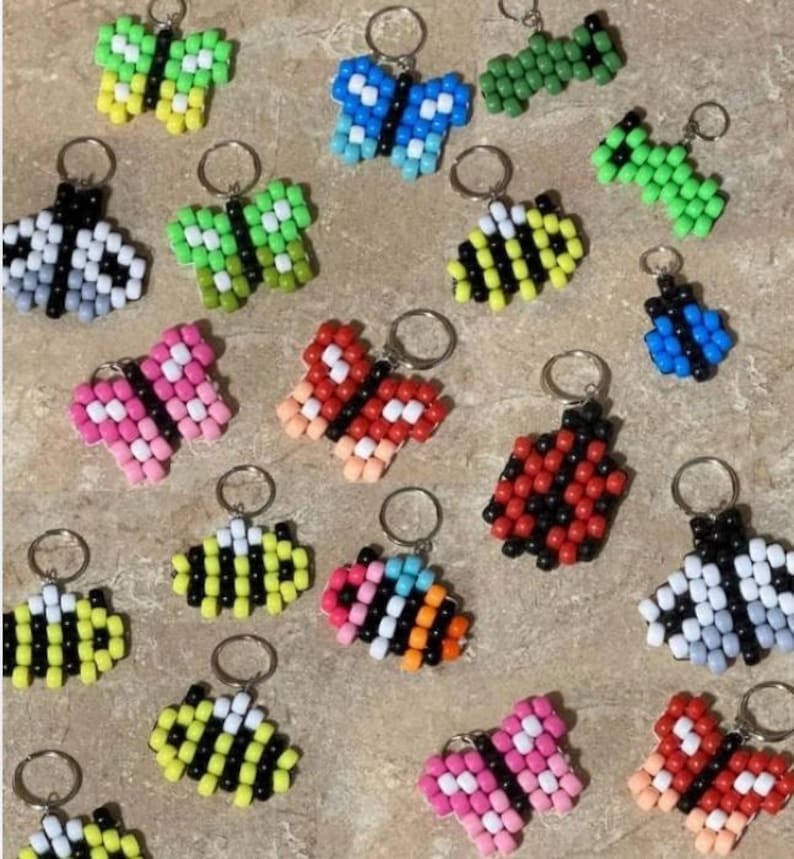 Puede incluir: Una colecci&oacute;n de llaveros coloridos hechos con cuentas de pl&aacute;stico. Los dise&ntilde;os incluyen varias mariposas, abejas y mariquitas en tonos rosa, azul, verde, amarillo, rojo, negro y blanco, cada uno unido a una anilla met&aacute;lica circular.