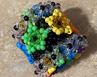 Può includere: Una scultura geometrica colorata di perline. La scultura è composta da perline di vari colori, tra cui verde, giallo, blu, nero e trasparente. Le perline sono disposte in un complesso motivo tridimensionale.