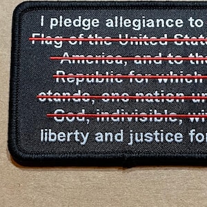 May include: Black patch with white text that reads "I pledge allegiance to the Flag of the United States of America, and to the Republic for which it stands, one nation under God, indivisible, with liberty and justice for all".  The words "Flag", "United States", "America", "Republic", "stands", "one", "God", and "indivisible" are crossed out with red lines.