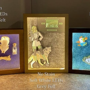 May include: Three illuminated shadow boxes with wooden frames. The left box has a light stain, navy blue felt, and contains various objects. The centre box has a no stain, grey felt, and a graphic. The right box has a dark stain, grey felt, and pins.
