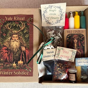 May include: A Yule Ritual box set containing items for winter solstice rituals. The box includes candles, incense, oil, and a Unakite crystal. The box features illustrations of a figure with antlers and the text "Yule Ritual" and "Winter Solstice".