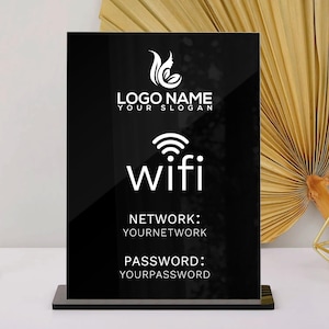 May include: A black acrylic WiFi sign with white text, including a logo, "wifi", and network/password details. The sign is on a white surface, with a gold candle holder and decorative fan in the background.