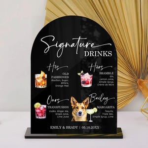 May include: An arched black acrylic sign titled Signature Drinks featuring illustrations of four cocktails and a dog. The text lists His Old Fashioned, Hers Bramble, Ours Transfusion, and Bailey Margarita, with the names Emily & Brady and 05.10.20XX.