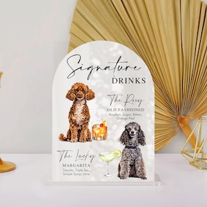 May include: A white sign with a black arch at the top. The sign says "Signature Drinks" and features two cocktails with illustrations of dogs. The first cocktail is called "The Roxy Old Fashioned" and the second is called "The Lucky Margarita".