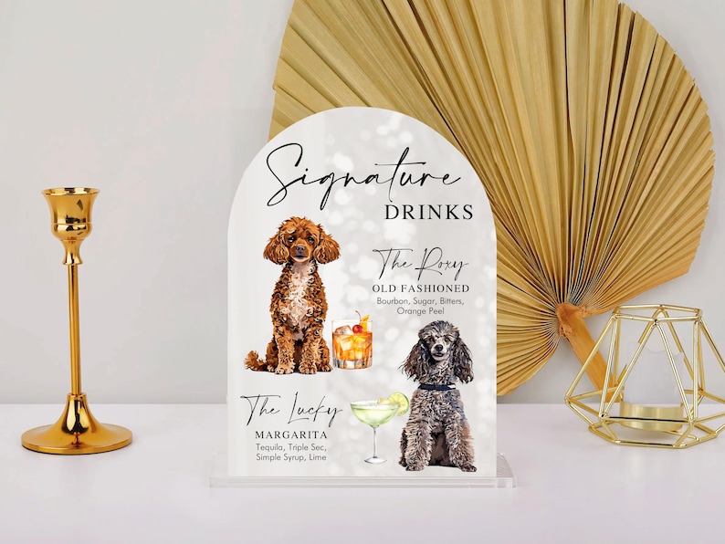 May include: A white sign with a black arch at the top. The sign says "Signature Drinks" and features two cocktails with illustrations of dogs. The first cocktail is called "The Roxy Old Fashioned" and the second is called "The Lucky Margarita".