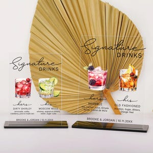 May include: Two acrylic signs with black text and illustrations of cocktails. The signs are labeled "Signature Drinks" and list the drinks "Dirty Shirley", "Moscow Mule", "Bramble", and "Old Fashioned".