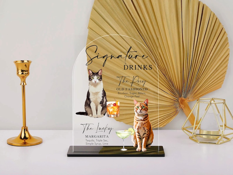 May include: A clear acrylic sign with a rounded top and black base. The sign features a black and white cat illustration and text that reads "Signature Drinks", "The Pory Old Fashioned", "Bourbon, Sugar, Bitters, Orange Peel", "The Lucky Margarita", "Tequila, Triple Sec, Simple Syrup, Lime".
