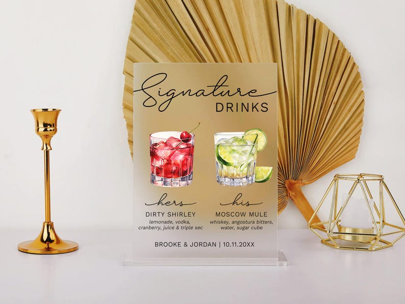 May include: A white acrylic sign with black text that reads "Signature Drinks". The sign features two watercolor illustrations of cocktails, one red and one green, with the text "hers" and "his" below each. The sign also includes the names of the cocktails, "Dirty Shirley" and "Moscow Mule", and their ingredients. The bottom of the sign reads "Brooke & Jordan | 10.11.20XX".