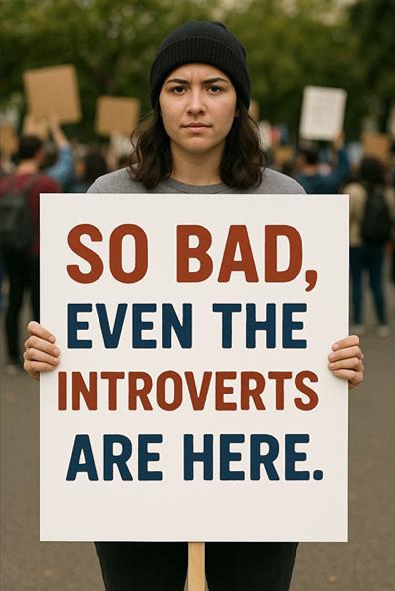 May include: A person wearing a black beanie and a grey shirt holds a white sign with the text "SO BAD, EVEN THE INTROVERTS ARE HERE." in red and blue lettering.
