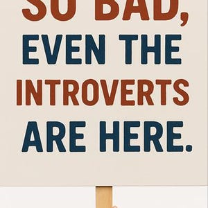 May include: A white sign with the text "SO BAD, EVEN THE INTROVERTS ARE HERE." in red and blue lettering. The sign is held by a hand.