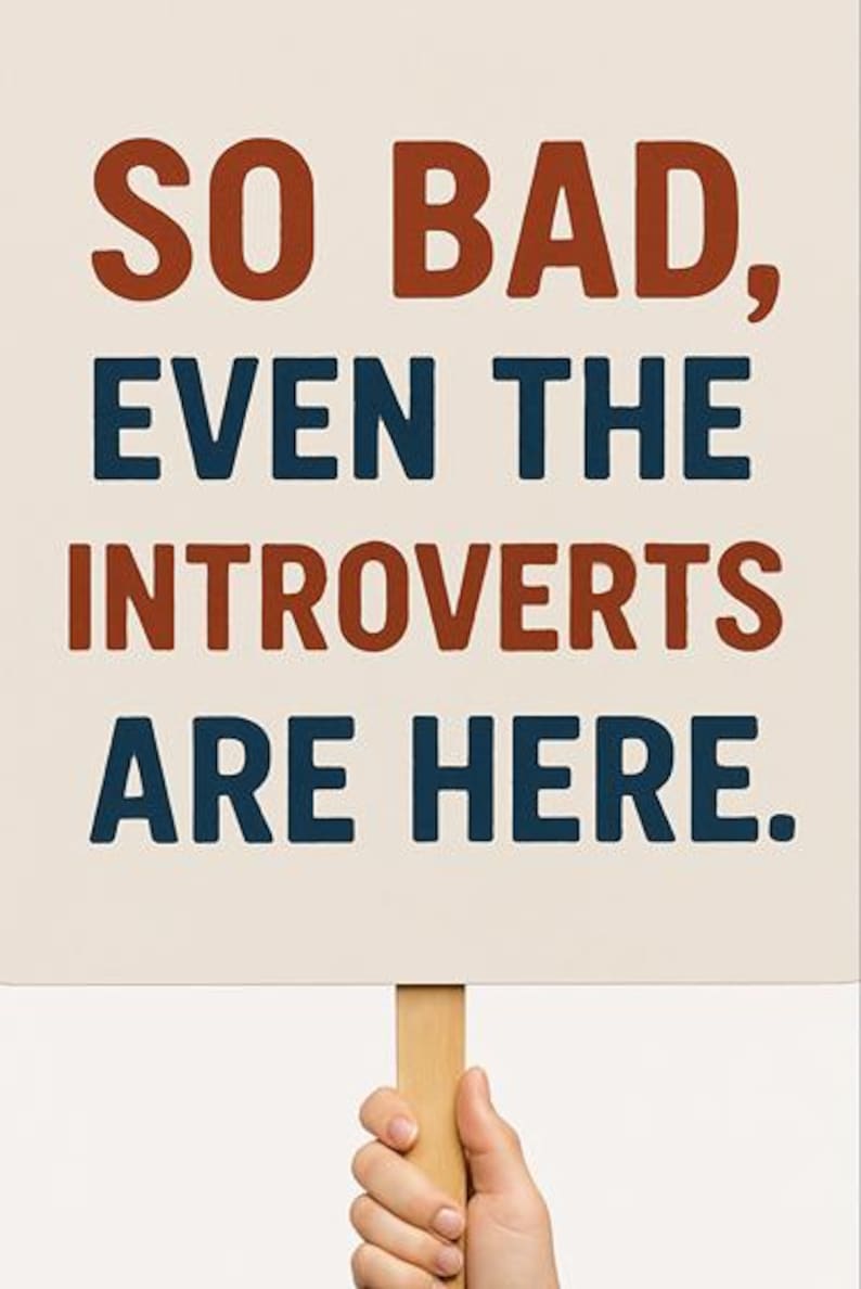 May include: A white sign with the text "SO BAD, EVEN THE INTROVERTS ARE HERE." in red and blue lettering. The sign is held by a hand.