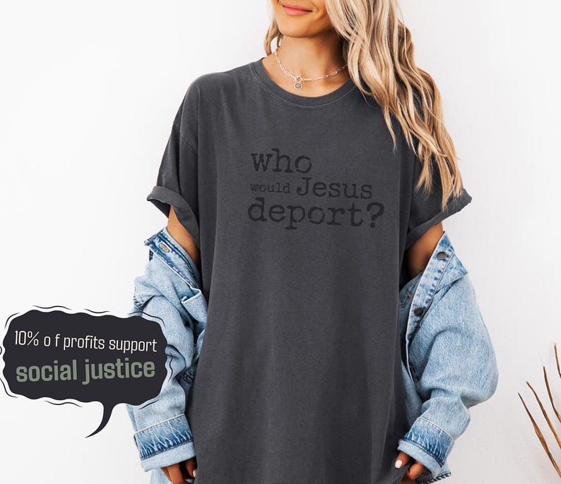 K&ouml;nnte beinhalten: Dunkelgraues T-Shirt mit dem schwarzen Text "who would Jesus deport?". Das Shirt wird mit einer hellblauen Jeansjacke getragen. Eine Sprechblase zeigt "10% of profits support social justice."