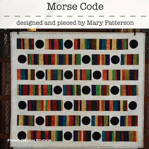 May include: A white quilt with a colorful striped pattern and black circles arranged in a Morse code pattern. The quilt is titled "Morse Code" and is designed and pieced by Mary Patterson.
