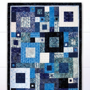 May include: A patchwork quilt with a geometric design in shades of blue and white. The quilt features squares and rectangles of varying sizes and patterns, with a dark blue border. The text "Fourteen Squared" is visible.