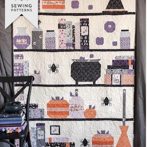 May include: A Halloween-themed quilt with a shelf design, featuring orange pumpkins, potion bottles, books, a witch's hat, and spiders against a cream background. The quilt is labelled "Spooky Shelfie Quilt".