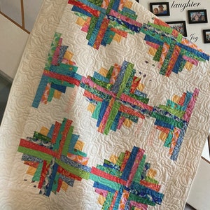 May include: A colorful handmade quilt with a log cabin design. The quilt features vibrant strips of fabric in shades of blue, green, pink, orange, and red, arranged in a geometric pattern against a white background. The quilt is quilted with a swirling pattern.