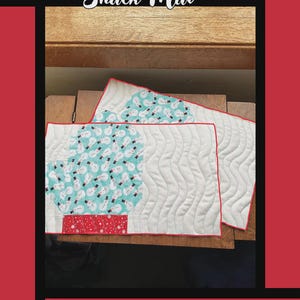 May include: Two quilted snack mats with a mitten design. One mat features a snowman pattern on a teal background, the other has a white background with wavy stitching. The mats have red trim and the text "Woolly Mitten Snack Mat".