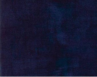 May include: A dark blue fabric with a subtle textured pattern. The fabric is a solid colour with a slight variation in shade. The fabric is shown with a ruler for scale.
