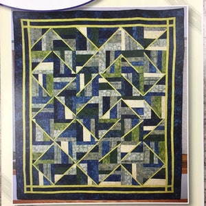 May include: A quilt pattern featuring a geometric design in shades of blue, green, and gray, framed by a dark blue border with a yellow accent. The text "Quilting on the Curve" and "Fiddlesticks" are also visible.