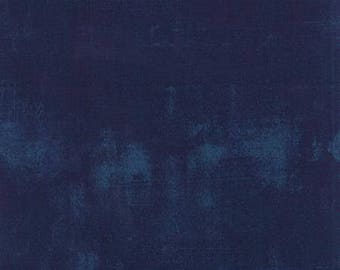 May include: A dark blue textured fabric with a distressed appearance. The fabric has a mottled effect with lighter blue areas, creating a vintage or worn look. The overall aesthetic is of a solid, yet complex, textile.